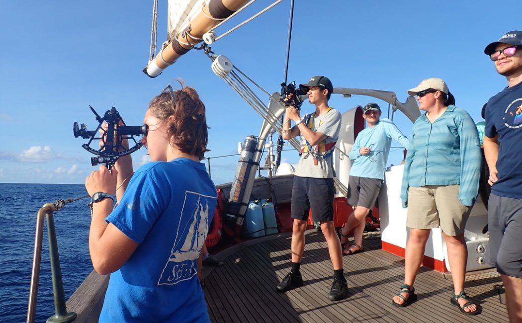 two people using a sextant on the deck of a large boat